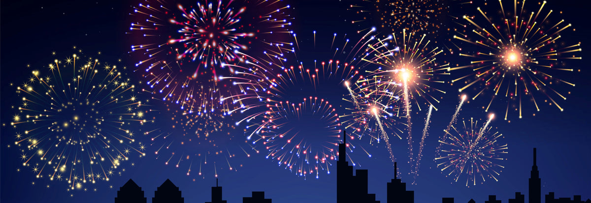 A night city skyline silhouette with colorful fireworks exploding across a dark blue sky.