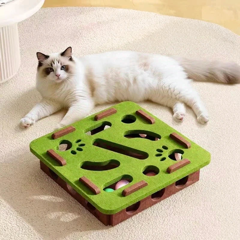 Two cats playing with a green and brown cat puzzle toy on a carpeted floor.