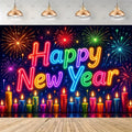 A New Year's Eve party backdrop featuring a dark background filled with colorful fireworks and the words 'Happy New Year' in glowing neon-style lettering. A row of lit candles in red, orange, yellow, green, blue, and purple sits along the bottom, with a light wood plank floor in front.