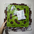 Green and brown puzzle mat with a white square object on top, held by a hand against a light background.