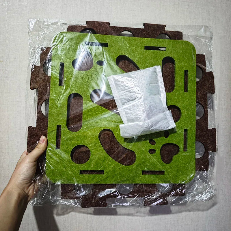 Green and brown puzzle mat with a white square object on top, held by a hand against a light background.