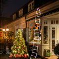 Decorative Christmas lights on a ladder outside a building with a Christmas tree and presents.