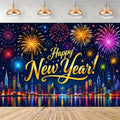 A New Year's Eve party backdrop banner featuring a vibrant fireworks and city skyline scene with 'Happy New Year!' written in gold script. The banner is shown hanging on a wall in a room mockup with hanging pendant lights above and a wooden floor below.