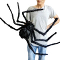 Person holding a large black spider prop against a white background