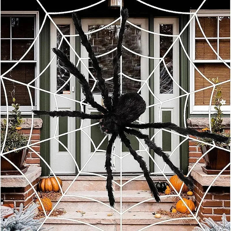 Large decorative spider on a spider web in front of a house entrance with pumpkins.