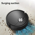 Robotic vacuum cleaner with 'Surging suction' text on a light surface with scattered debris.