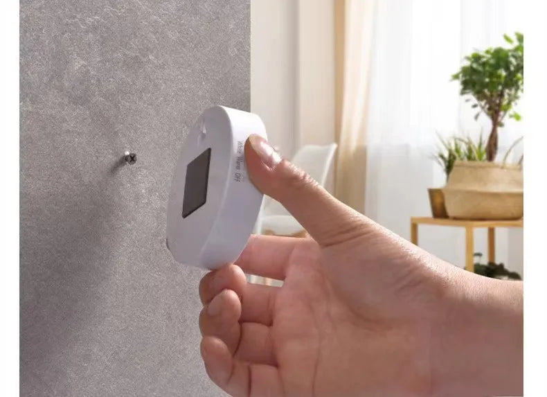 Hand installing a white thermostat on a gray wall with a blurred indoor background