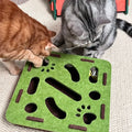 Two cats playing with a green and brown cat toy on a carpeted floor.