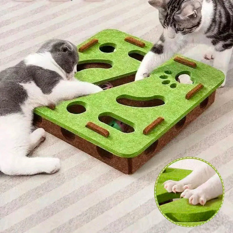 Two cats playing with a green and brown cat puzzle toy on a carpeted floor.