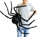 Person holding a large black spider prop against a white background