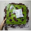 Green and brown interlocking foam puzzle mat with a white cloth inside, held by a hand against a light gray background.